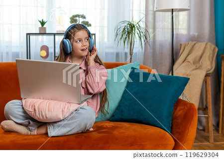 Child girl in headphones using laptop listens to music or lesson distance learning education at home 119629304