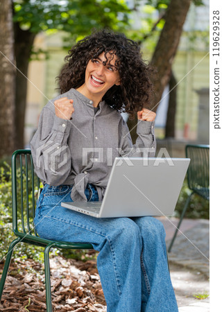 Caucasian happy woman working on laptop celebrate success win money sitting on urban street in city Caucasian happy woman working on laptop celebrate success win money sitting on urban street in city 119629328
