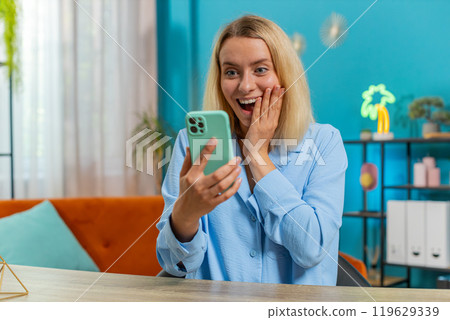 Woman freelancer using mobile smartphone receive good news celebrate victory win at home office 119629339