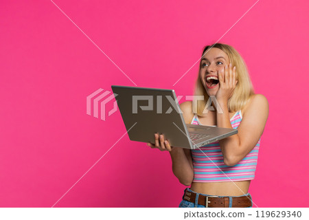Excited happy young woman working on laptop winning online lottery game celebrating success victory 119629340