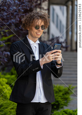 Happy businessman using smartphone typing text answering e-mail messages online mobile app outdoors 119629343