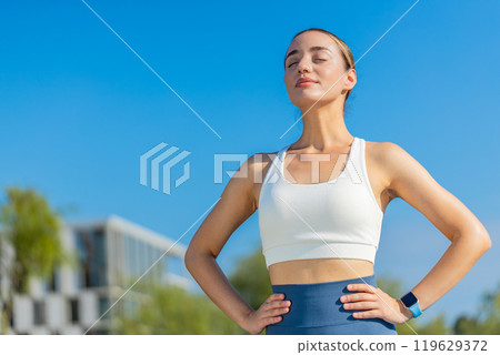 Young Caucasia female runner is short of breath after a fast sprint run in urban city park sunny day 119629372