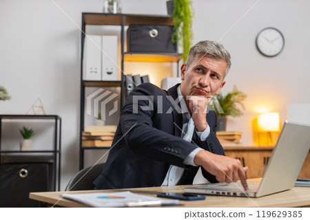 Young businessman using laptop while thinking about important creative project decision at desk 119629385