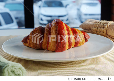 Golden brown croissant sits invitingly on a plate beside a textured linen napkin in a cozy setting 119629912