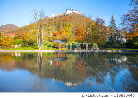 The imposing Bezdez Castle rises majestically above a tranquil lake, surrounded by vibrant autumn foliage, reflecting the historic Gothic architecture and serene landscape. The imposing Bezdez Castle rises majestically above a tranquil lake, surrounded by vibrant autumn foliage, reflecting the historic Gothic architecture and serene landscape. 119630446