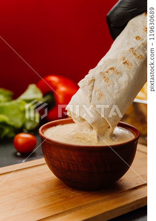 Dipping a wrap into creamy sauce, the perfect blend of flavors for food lovers Dipping a wrap into creamy sauce, the perfect blend of flavors for food lovers 119630689