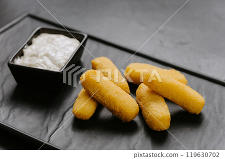 Golden crispy cheese sticks with a creamy dip, served on a sleek black plate. Perfect appetizer 119630702