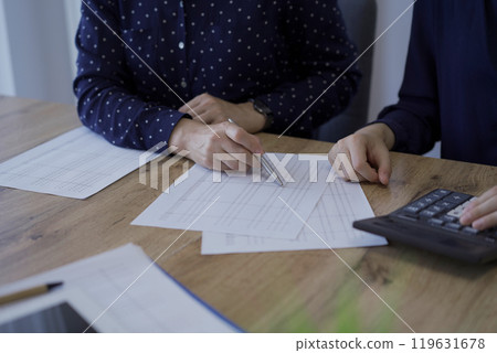 Accountants or auditors reviewing financial documents while sitting at the wooden desk in office. Professionals analyzing paper reports and using calculators, close up view. Audit and taxes Accountants or auditors reviewing financial documents while sitting at the wooden desk in office. Professionals analyzing paper reports and using calculators, close up view. Audit and taxes 119631678