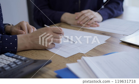 Accountants or auditors reviewing financial documents while sitting at the wooden desk in office. Professionals analyzing paper reports and using calculators, side view. Audit and taxes 119631718