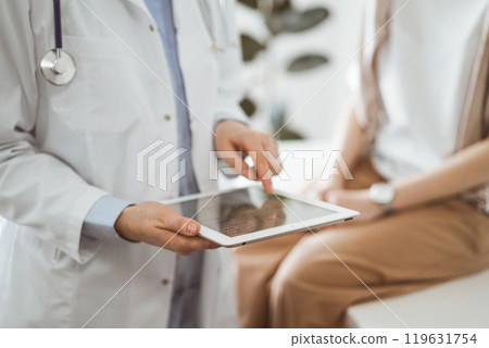 Doctor and patient in clinic. Friendly physician using tablet computer near a young woman. Medicine concept 119631754