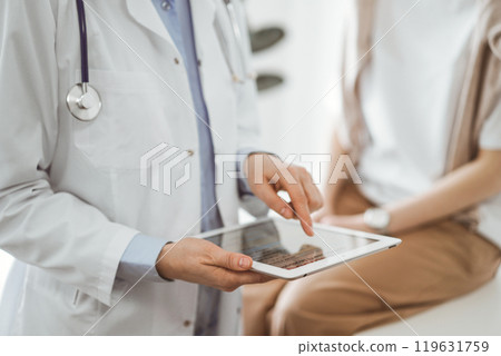 Doctor and patient in clinic. Friendly physician using tablet computer near a young woman. Medicine concept 119631759
