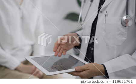 Doctor and a patient. The female physician is pointing into tablet computer besides a young woman during a consultation in the clinic. Medicine concept Doctor and a patient. The female physician is pointing into tablet computer besides a young woman during a consultation in the clinic. Medicine concept 119631761