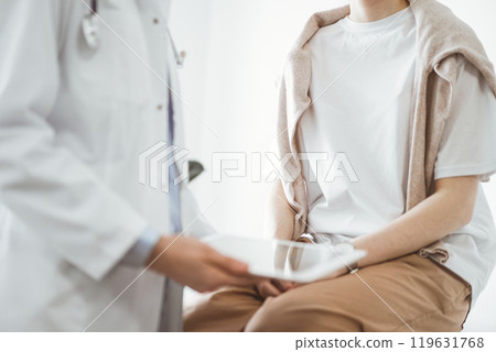 Doctor and patient in clinic. Friendly physician using tablet computer near a young woman. Medicine concept Doctor and patient in clinic. Friendly physician using tablet computer near a young woman. Medicine concept 119631768
