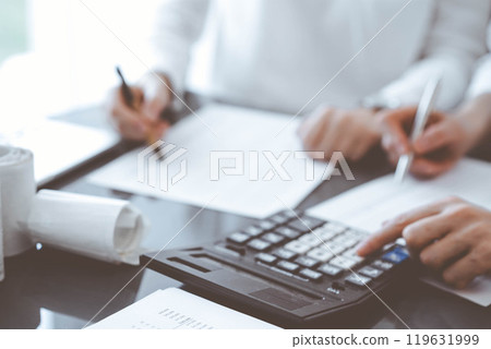 Two accountants use a calculator and laptop computer for counting taxes or revenue balance. Business, audit, and taxes concepts Two accountants use a calculator and laptop computer for counting taxes or revenue balance. Business, audit, and taxes concepts 119631999