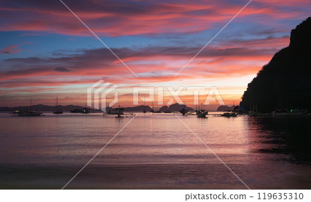 Sunset view over calm waters with boats anchored near the shoreline in a tropical location. El NIdo, Palawan. Sunset view over calm waters with boats anchored near the shoreline in a tropical location. El NIdo, Palawan. 119635310