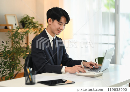 Smiling young businessman working with laptop at office Smiling young businessman working with laptop at office 119638990