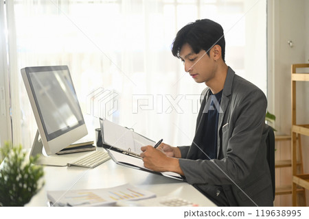 Concentrated businessman working with business reports and data at office Concentrated businessman working with business reports and data at office 119638995