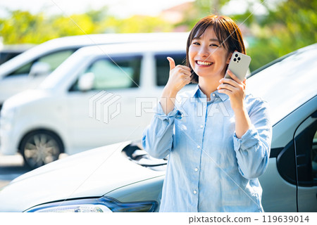 A woman making a phone call on her smartphone next to her car 119639014