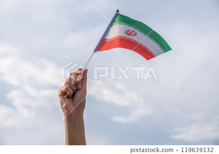 Someone hand holding and waving an Iranian flag against the sky. 119639132