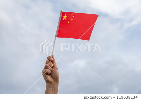 Someone hand holding and waving a flag of China against the sky. 119639134