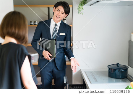 一位來自房屋建築商的男性規劃師/銷售人員和一位女性客戶介紹系統廚房的抽屜儲存。 一位來自房屋建築商的男性規劃師/銷售人員和一位女性客戶介紹系統廚房的抽屜儲存。 119639156