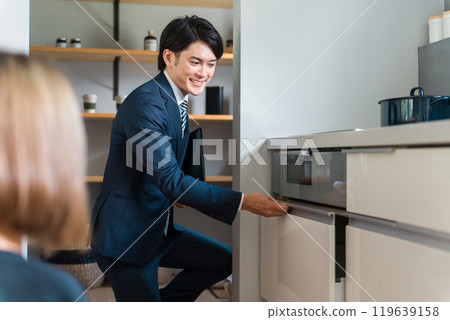 一位來自房屋建築商的男性規劃師/銷售人員和一位女性客戶介紹系統廚房的抽屜儲存。 一位來自房屋建築商的男性規劃師/銷售人員和一位女性客戶介紹系統廚房的抽屜儲存。 119639158