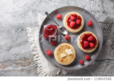 British Crumpets breakfast with butter and raspberry jam closeup on the plate. Horizontal top view British Crumpets breakfast with butter and raspberry jam closeup on the plate. Horizontal top view 119643588