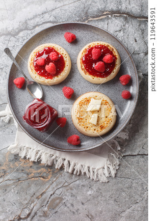 Hot Toasted Crumpets with piece of butter and raspberry jam closeup on the plate. Vertical top view 119643591