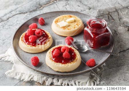 Hot fresh breakfast crumpets with butter melting, jam and fresh raspberries closeup on the plate. Horizontal 119643594