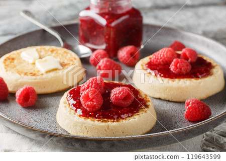 Hot Toasted Crumpets with piece of butter and raspberry jam closeup on the plate. Horizontal 119643599