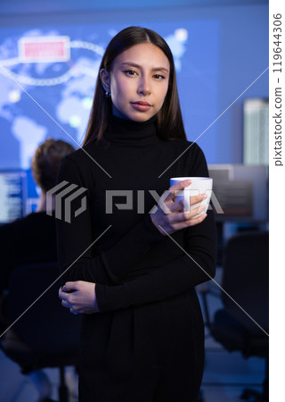 Confident Female Cybersecurity Analyst or Manager in large Cyber Security Operations Center SOC handling Threats 119644306