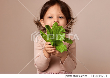 smiling child girl holding fresh green salad on beige background. focus on salad smiling child girl holding fresh green salad on beige background. focus on salad 119644701