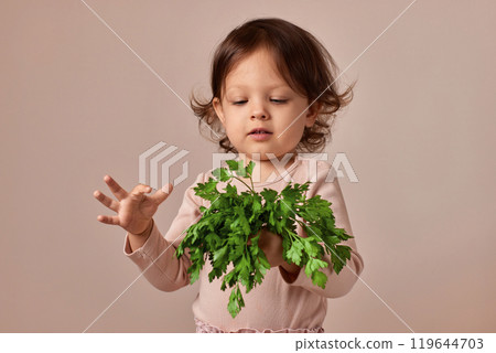 little child girl with fresh green parsley on beige background. healthy baby food. 119644703