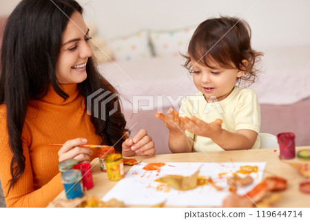 happy little child girl and mom spending good time painting hands and autumn yellow leaves together 119644714