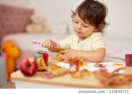 happy little child girl painting autumn leaves. baby girl drawing leaves in yellow paint happy little child girl painting autumn leaves. baby girl drawing leaves in yellow paint 119644731