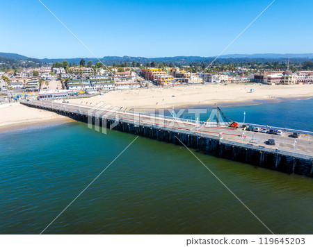 Aerial view of Santa Cruz, California, featuring the Santa Cruz Wharf, sandy beach, vibrant town buildings, and distant hills under a clear sky. Aerial view of Santa Cruz, California, featuring the Santa Cruz Wharf, sandy beach, vibrant town buildings, and distant hills under a clear sky. 119645203