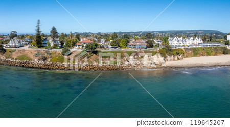 Aerial view of Santa Cruz, California, featuring a rocky shoreline, sandy beach, cliffs, and charming houses. Lush greenery and hills in the background. 119645207