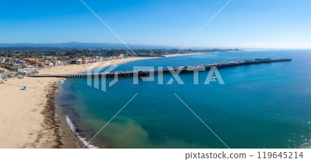 Aerial view of Santa Cruz, California, featuring the Santa Cruz Wharf, sandy beach, vibrant boardwalk, lush greenery, and a solitary sailboat. 119645214