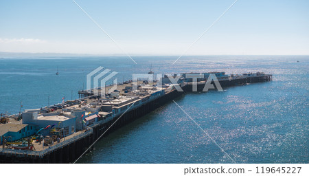 The image captures Santa Cruz Wharf with buildings and shops, surrounded by boats in the Pacific Ocean under a clear blue sky in Santa Cruz, California. 119645227