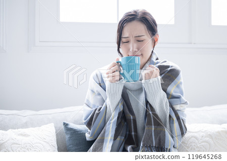 Do I have a cold? A woman drinking a hot drink with a headache and chills, perhaps the beginning of a cold, close-up Do I have a cold? A woman drinking a hot drink with a headache and chills, perhaps the beginning of a cold, close-up 119645268