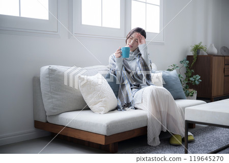 Do I have a cold? A woman drinking a hot drink, feeling chilly, perhaps due to the beginning of a cold. Wide-angle 119645270