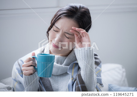 Do I have a cold? A woman drinking a hot drink with a headache and chills, perhaps the beginning of a cold, close-up 119645271