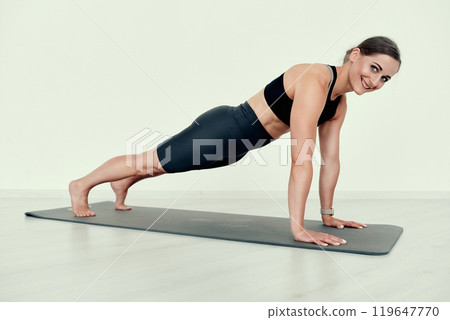 Smiling Fitness Trainer in Plank Position on Yoga Mat Smiling Fitness Trainer in Plank Position on Yoga Mat 119647770