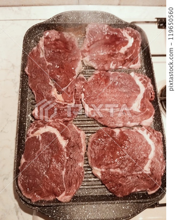Raw rib eye steak cooking on the griddle. Close up red meat Raw rib eye steak cooking on the griddle. Close up red meat 119650560