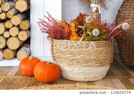 Woven basket brimming with vibrant dried flowers and plants,  two small orange decorative pumpkins 119650779