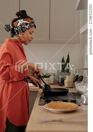 Hispanic Woman Cooking Pancakes on Stove in Kitchen 119652205
