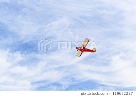 Red single-engine ultralight airplane flying in the blue sky with white clouds Red single-engine ultralight airplane flying in the blue sky with white clouds 119652257