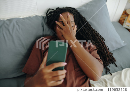Woman Relaxing on Bed While Holding Smartphone Woman Relaxing on Bed While Holding Smartphone 119652528