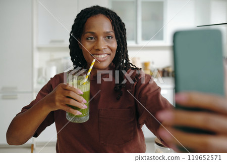 Smiling Woman Drinking Green Smoothie at Home Kitchen 119652571