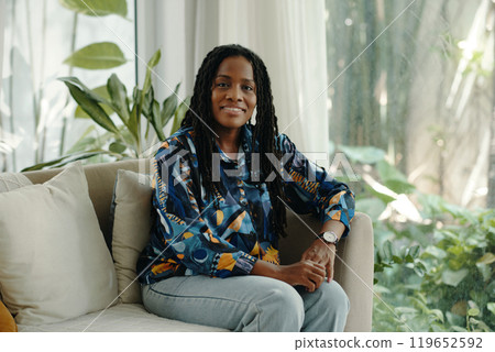 Smiling Woman Sitting on Couch in Bright Living Room Smiling Woman Sitting on Couch in Bright Living Room 119652592